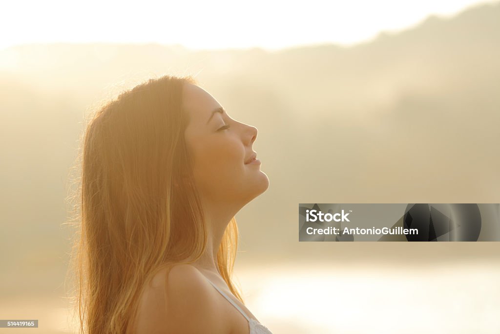 Woman breathing deep fresh air in the morning sunrise Backlight profile of a woman breathing deep fresh air in the morning sunrise isolated in white above Inhaling Stock Photo