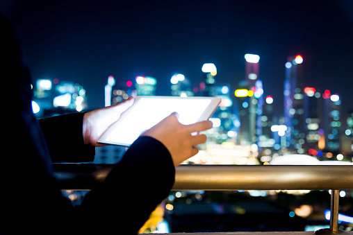 Businesswoman using digital tablet with city skyline night light background.