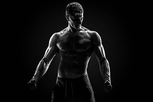 Sexy muscular man posing with naked torso on black background Sexy muscular man posing with naked torso in studio and looking behind on black background. Black and white body building stock pictures, royalty-free photos & images