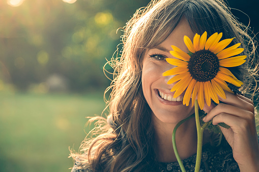 Girl in park smiling and covering face with sunflower