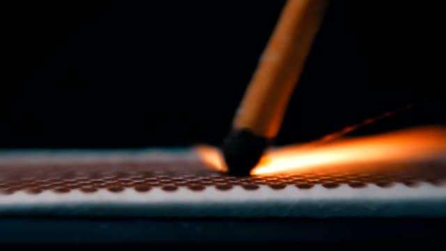 The match moves on the side of the matchbox and light the fire. Macro
