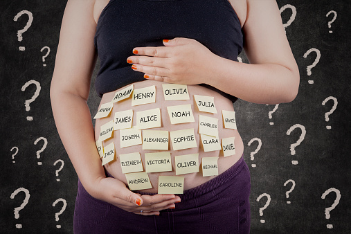 Pregnant woman's belly with baby names and question mark symbolizing a decision for making baby names