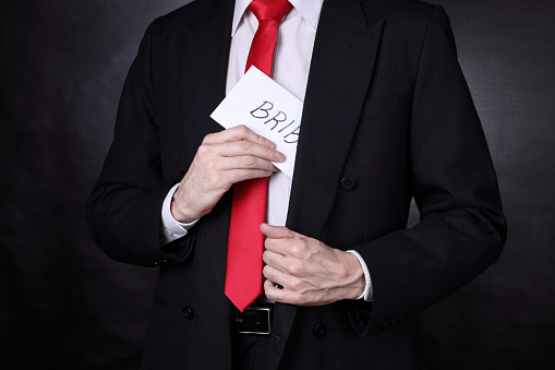 Unrecognizable man wearing a black suit and red necktie has a bribe in his pocket