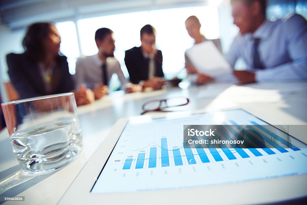 Business meeting Close-up of touchpad with graphics on the table with people in the background Business Finance and Industry Stock Photo