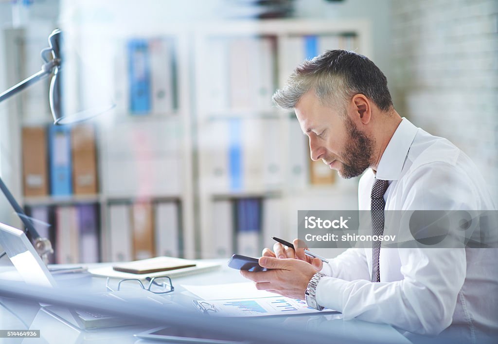 Using smartphone at workplace Mature businessman texting in his office Office Stock Photo