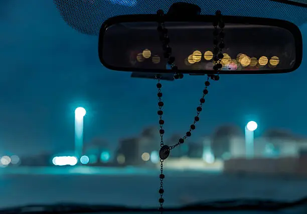 Rear view mirror with rosary on it which shows the