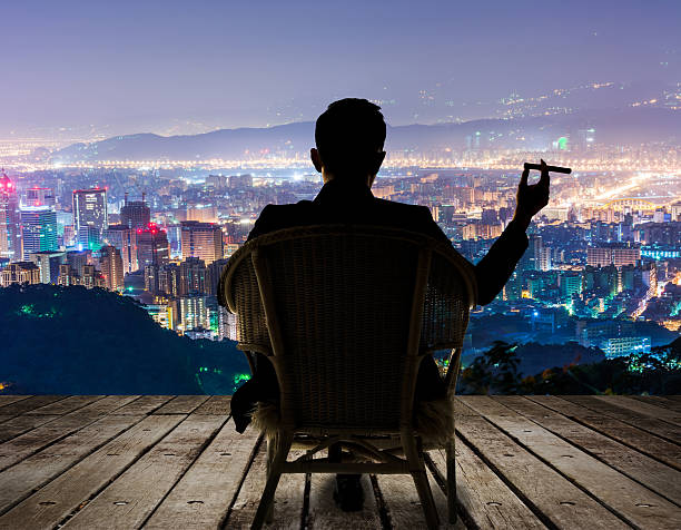 successful businessman Silhouette of businessman sit on chair and hold a cigar and looking at the city in night. rich man stock pictures, royalty-free photos & images