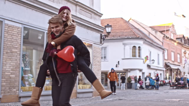 Slow motion camera stabilization shot of a young man spinning while he is carrying piggyback his girlfriend with a heart shaped balloon. Also available in 4K resolution.