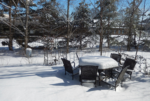 Backyard furniture, table and chairs on a patio covered with a thick layer of snow on a bright winter day