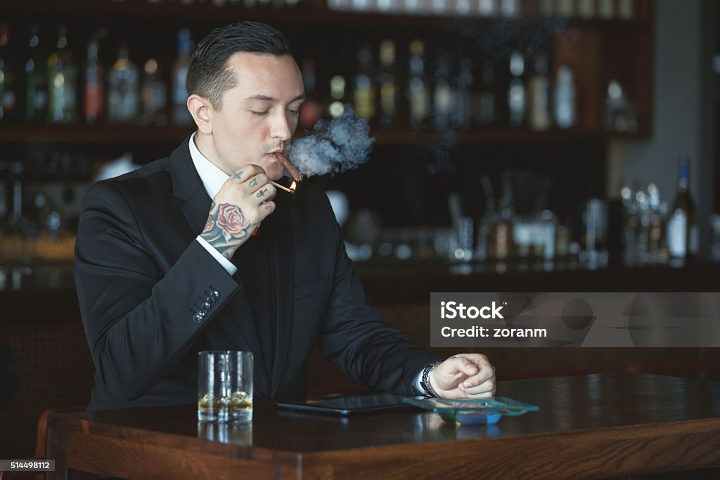 Businessman lighting his cigar Businessman lighting his cigar in a bar, copy space Tattoo Stock Photo