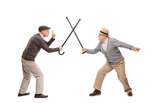 Studio shot of two senior gentlemen having a sword fight with their canes isolated on white background