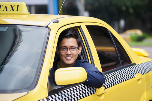 Portrait of happy chinese taxi driver in yellow car smiling and looking at camera