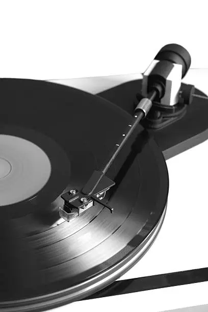 Vintage turntable in silver case playing a vinyl record. Vertical black and white photo isolated on white background closeup
