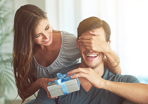 A young woman covering her husband's eyes for a surprise gift