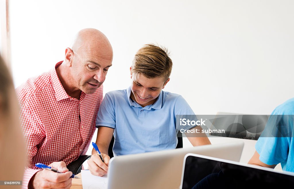 Knowledge Is Power Adult male tutor helping a male student at his home school with his writing homework at his desk. Adult Student Stock Photo