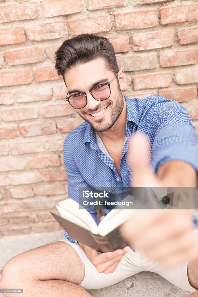 this book is good! seated young student reading a book and making the ok thumbs up sign Adult Stock Photo