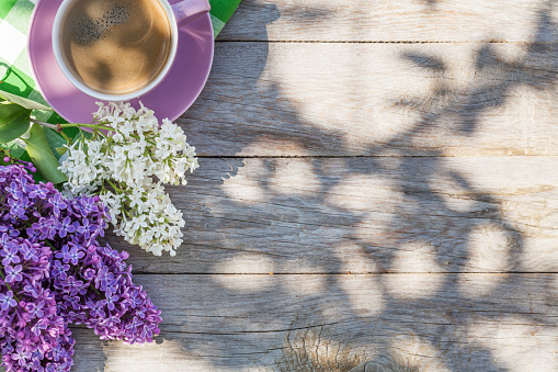 Coffee cup and colorful lilac flowers on garden table. Top view with copy space
