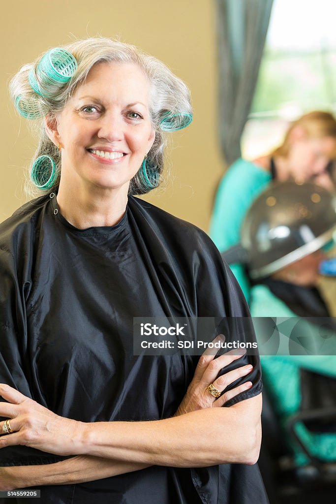 Senior salon customer smiling while having hair styled with rollers Happy senior woman talking with friend in beauty salon Gray Hair Stock Photo