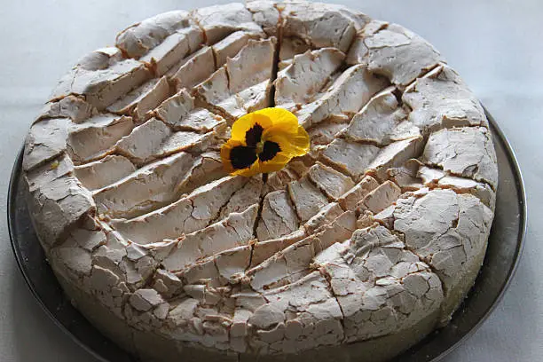 Photo showing a homemade blueberry cooked cheesecake with a crunchy meringue topping, decorated with a yellow edible pansy flower and cut into slices, ready to be served.