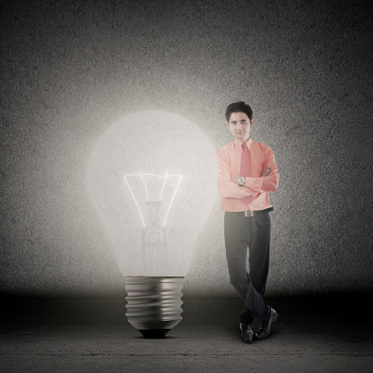 Businessman is standing beside bright light bulb on black background
