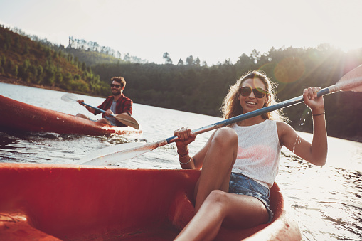 Beautiful young woman kayaking in a lake with man paddling in the background. Young couple canoeing on summer day.