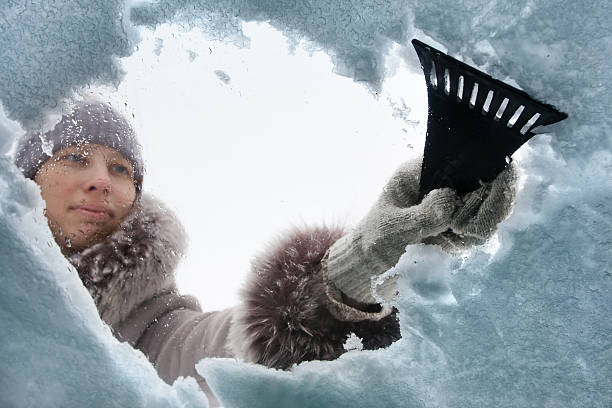 woman cleaning window of car from the snow with scraper woman cleaning snow-covered car with a scraper car snow stock pictures, royalty-free photos & images