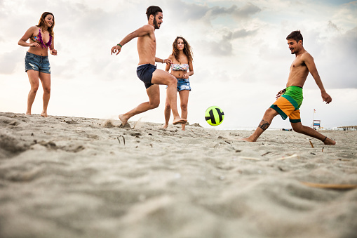 Friends playing soccer on the beach during summer vacations at dusk.