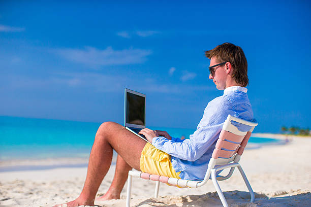 istock Young man working on laptop at tropical beach 514583899
