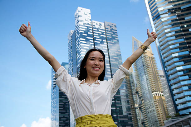 Asian Business woman celebrating victory Young Asian female business professional stretching hands to celebrate business triumph, posing in front of office buildings. stars in your eyes stock pictures, royalty-free photos & images