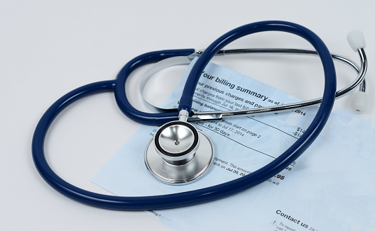 A stethoscope, a billing statement and various medicines representing the cost of medical care.