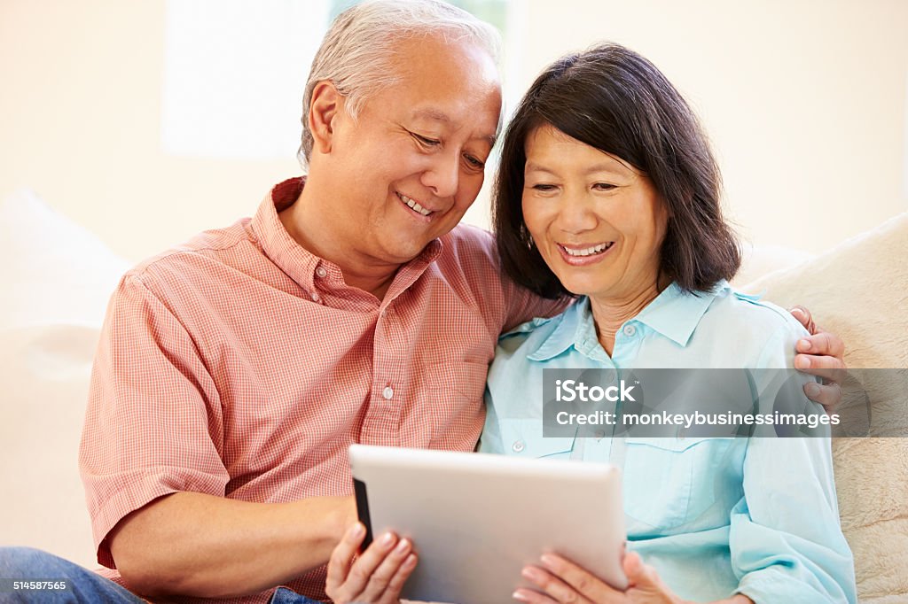 Senior Couple Sitting On Sofa Using Digital Tablet Senior Couple Sitting On Sofa Using Digital Tablet Smiling Senior Couple Stock Photo