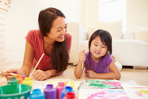 Mother And Daughter Lying On Floor And Painting Picture Smiling