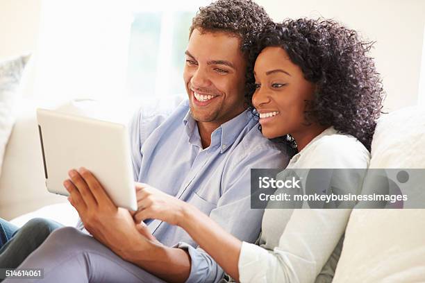 Young Couple Sitting On Sofa Using Digital Tablet Stock Photo - Download Image Now - Digital Tablet, Couple - Relationship, African-American Ethnicity