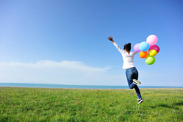 young asian woman running and jumping with colored balloons