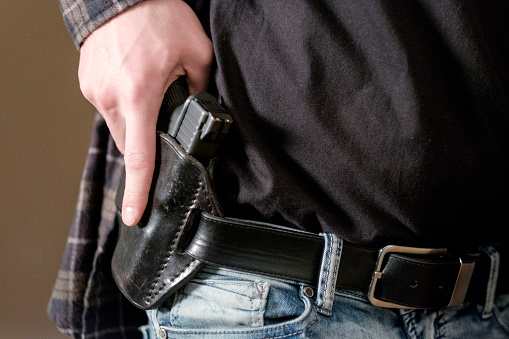 A man drawing a gun from a leather holster on his belt.