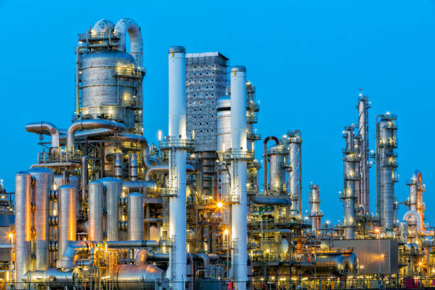 Petrochemical Plant Illuminated at Dusk A large, modern petrochemical plant at dusk in industrial district near Rotterdam, Netherlands, Benelux, Europe. Many chimneys, tanks, distillation towers and other installations are visible against blue sky. 50 megapixel HDR image taken with Canon EOS 5Ds, digital blending technique, long exposure with tripod. smoke stack photos stock pictures, royalty-free photos & images
