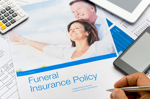 Close up of a funeral insurance kit. It is on an office desk with other paperwork. There are also a digital tablet and mobile phone on the desk. There is an image of a happy mature couple on the cover, The included image can be found in my portfolio. Image  # 16596262