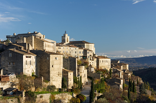 Gordes in the warm light of a winter afternoon. Gordes is a small medieval village on a hill. Blue sky in the background. French department Vaucluse, Provence-Alpes-Cote d'Azur, Southern France, in the North of the Luberon. Near the small town L'Isle-sur-la-Sorgue, 40 km east of Avignon. A famous travel destination in Southern France.