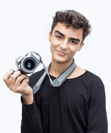 Smiling child posing with his digital camera and standing over isoalted white background. Studio shot. Teenage boy looking at camera in happiness. Vertical composiiton. Child's ethnicity belongs to Turkish, middle eastern ethnicity.