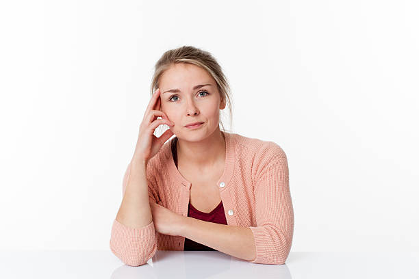 reflection concept - concerned beautiful young blond woman sitting at a sparse desk for patience and quietness, white background studio
