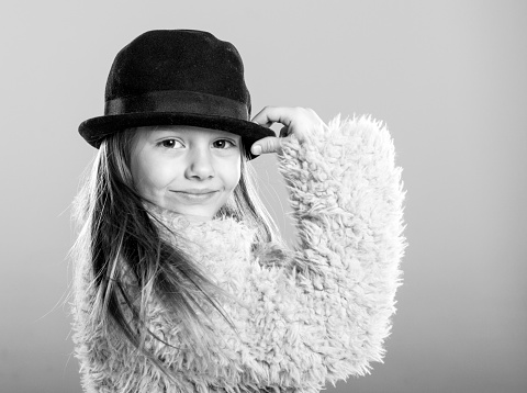 Adorable little girl in a black and white studio shot, wearing a coat and black hat, smiling and looking at camera.