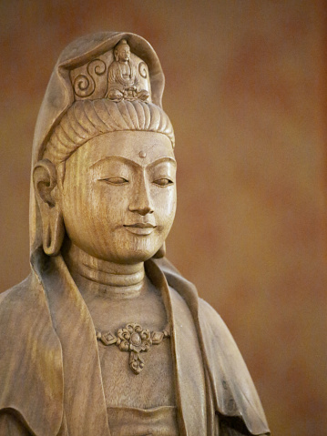 Soft Quan Yin wooden statue sits peacefully against burnt orange background.