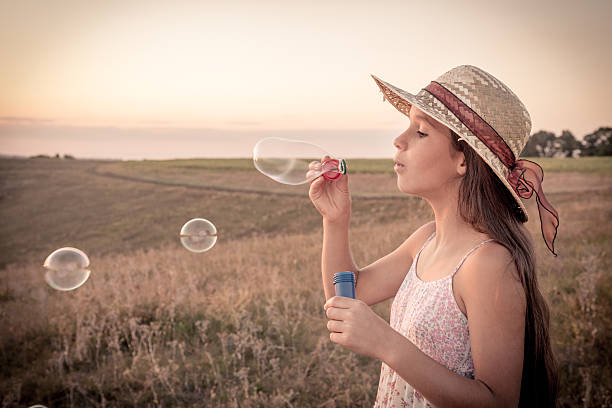 Girl in hat blowing up the soap bubbles on sepia toned landscape