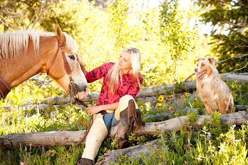 A cowgirl sits resting with her horse and dog, Parade Rest Ranch, Montana, USA. 