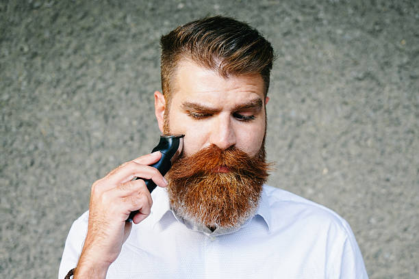 Portrait Of Bearded Man Trimming His Beard Portrait of bearded man trimming his beard. frowning headshot close up studio shot stock pictures, royalty-free photos & images