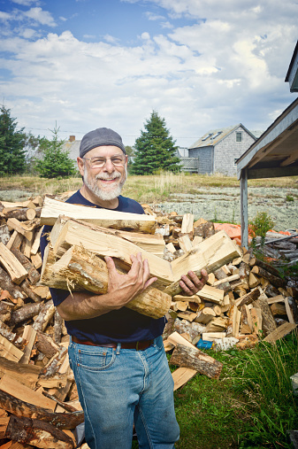 Senior Man Working Piling Firewood in rural Nova Scotia.  Man has a grey beard and work clothes.  Stock photo taken with a Leica M9 camera.