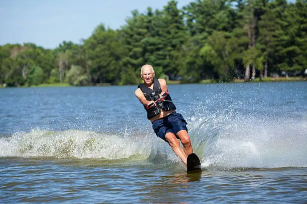 A 74 year old senior man is staying active, slalom water skiing on a Summer lake. Focus is on the rope knot near the handle, at 100% the man is slightly soft.