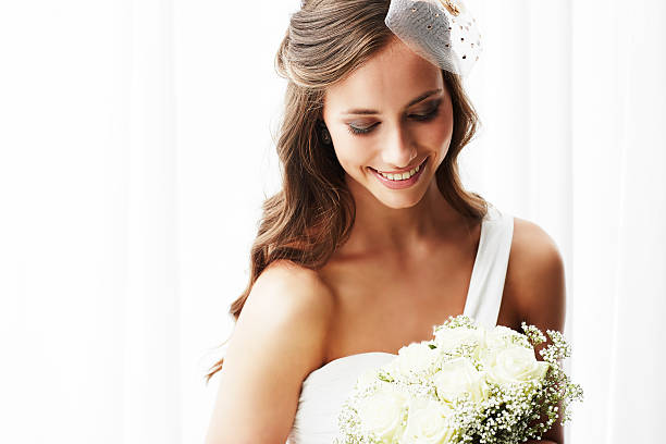 Young bride in wedding dress holding bouquet, studio shot stock photo