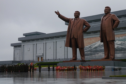 Pyongyang, North Korea - August 15 2012: North Korean soldiers showing their respect to their political leaders at the Grand Monument on Mansu Hill with the bronze statues of Kim II Sung and Kim Jong II.