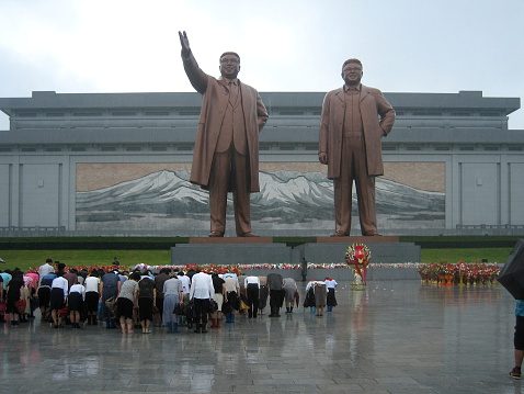 Pyongyang, North Korea - August 15 2012: North Koreans showing their respect to their political leaders at the Grand Monument on Mansu Hill with the bronze statues of Kim II Sung and Kim Jong II.